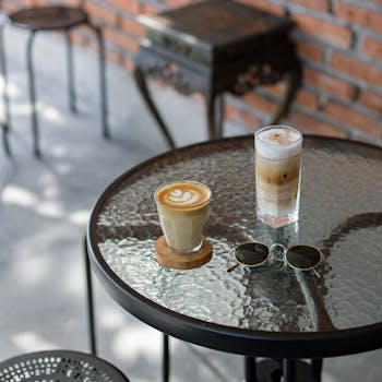 A chic cafe setup with lattes and sunglasses on a glass table, perfect for a relaxing brunch.